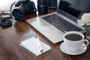 workplace of a photographer with laptop, camera, lenses coffee cup and notepad on a wooden table,  copy space - obrazy, fototapety, plakaty