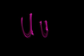 Long exposure photograph of  the letter u in pink neon color, in upper case and lower case, parallel lines pattern against a black background. Light painting photography.