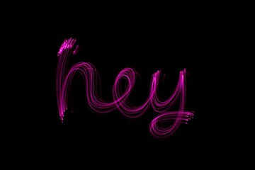 Long exposure photograph of the word 'hey' in pink neon colour in an abstract swirl pattern against...