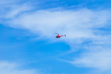 Red helicopter flying in the sky. Small red helicopter in the blue sky