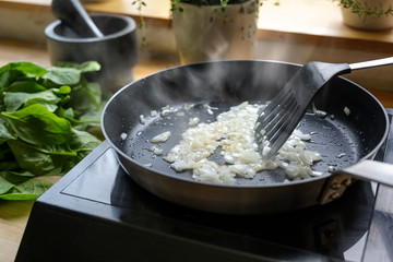 onions are fried with a lot of steam in a black pan, cooking and kitchen concept