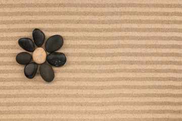 Stone flower. Flower made of stones on the striped sand background.