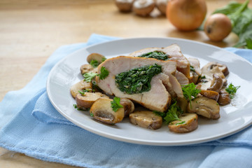 chicken breast fillet stuffed with spinach, served with mushrooms and parsley garnish on a blue napkin and a light wooden table, copy space, selected focus, narrow depth of field