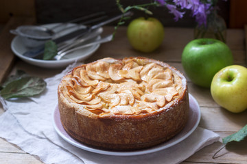 Pie with apple cream filling, apples and dishes on a wooden background. Rustic style.