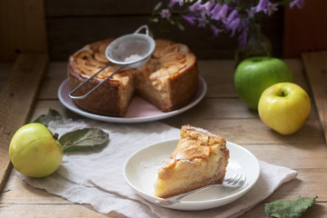 Pie with apple cream filling, apples and dishes on a wooden background. Rustic style.
