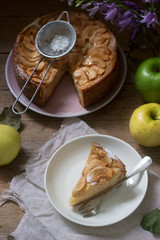 Pie with apple cream filling, apples and dishes on a wooden background. Rustic style.