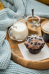 Blaubeermuffin mit Kaffee, Milch und Zucker auf Holztablett und gemütliches Sofa mit blau Wolldecke und gelb Kissen 