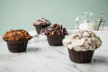 Muffin Auswahl mit Blaubeeren, Walnuss, Haselnuss und Weiße Schokolade mit Milch und Zucker für Kaffeepause auf Marmor Tisch und Grün Hintergrund