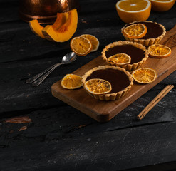 chocolate orange tartlets on a wooden board, dark background, cinnamon stick, dessert