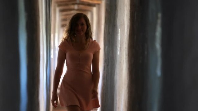 Young girl woman in pink dress walking in slow motion with focus rack shift blur in fortress tunnel passage in Italy during summer with walls and windows in Castiglione del Lago