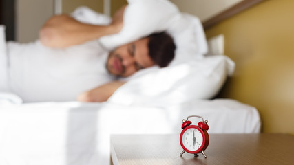 Exhausted man being awaken by alarm clock in his bedroom