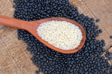 Wooden spoon with raw rice over heap of beans