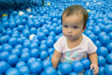 Fototapeta na wymiar Asian kid in blue ball pond. Baby playing in dry ball pond indoor playground.