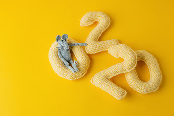 Happy New Year 2020. Number 2020 knitted from yarn and gray toy mouse symbol of year on bright yellow background, cheese color. Flat lay, top view, copy space