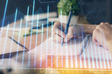 Financial forex graph drawn over hands taking notes background. Concept of research. Multi exposure