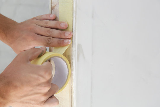 Man putting tape on the wall. The simple step for the quick and easy painting process. Renovation house concept.	