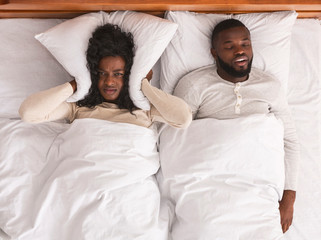 Woman covering ears with pillow, can not handle snoring husband
