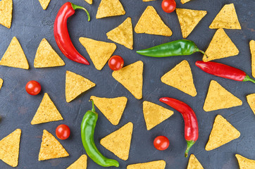 Nachos-yellow corn chips, red and green peppers, tomatoes, on a dark background. The concept of Mexican food. The view from the top.