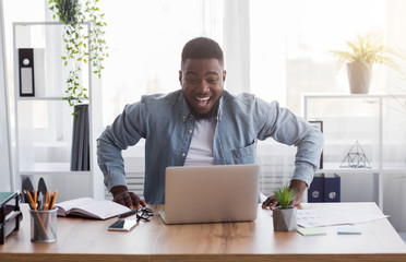 Joyful black employee looking at laptop screen with excitement