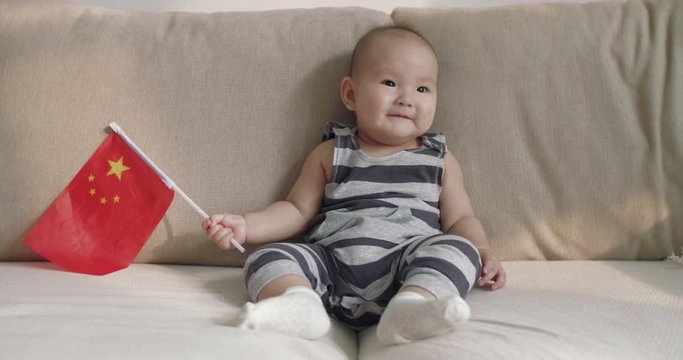 Happy Chinese baby infant girl holding China natinal flag sitting in sofa