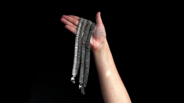 A single female hand comes up and shoes a bunch of payals, anklets, ankle chain, ankle bracelet or ankle string in her hands isolated on black background.