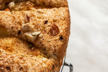 Sponge cake with apples, crushed walnuts and cinnamon lies on a metal stand on a light background, on the right is an empty place, close-up