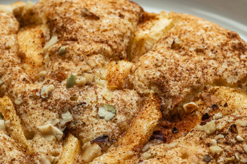 Sponge cake with apples, crushed walnuts and cinnamon lies on a white plate, close-up, side view from above