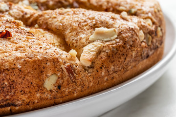 Sponge cake with apples, crushed walnuts and cinnamon lies on a white plate on a light background, close-up