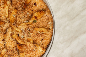 Sponge cake with apples, crushed walnuts and cinnamon lies on a white plate on a light background, on the right is an empty place, close-up
