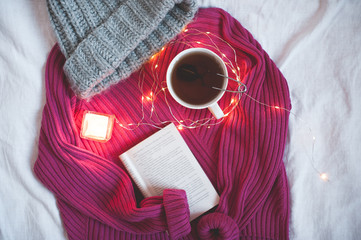Mug of tea with open book and knitted sweater in bed closeup. Top view. Good morning.