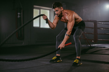 Hard exercises with ropes athletic man practicing cross fit training he make concentrated face while doing his workout