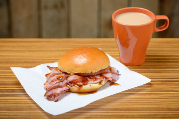 Bacon roll with a mug of tea and brown sauce with copy space