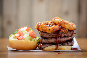 Open triple stack beef burger with onion rings, salad and bbq sauce