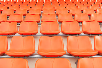 Rows of empty orange plastic grandstand seats at stadium.