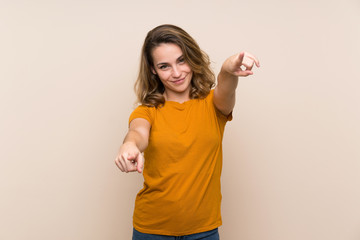 Young blonde girl over isolated background points finger at you while smiling