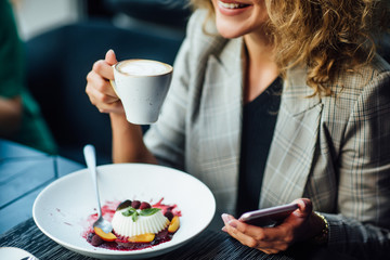 Close up photo, young woman resting in restaurant with cup of latte and dessert on table.