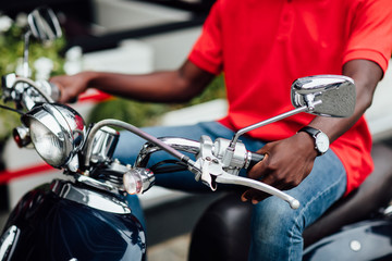 Close up photo.  Rider biker guy wearing red shirt and sitting on classic style cafe racer motorcycle. Bike custom. Brutal fun urban lifestyle. Outdoor portrait.