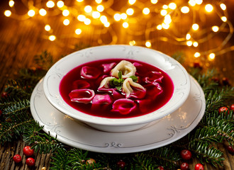 Fototapeta Christmas beetroot soup, red borscht with small dumplings with mushroom filling in a ceramic white plate on a wooden table.Traditional Christmas eve dish in Poland.  obraz