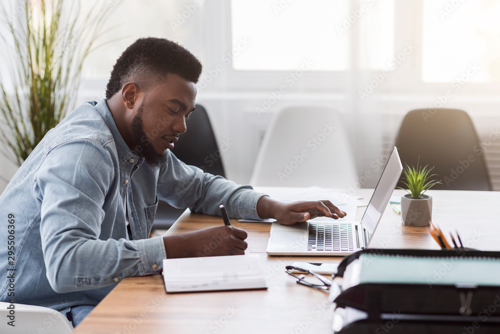 Poster Employee using laptop and taking notes while working in office