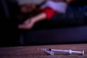 Close-up on the floor of the syringe with the drug. young woman desperate drug addict in the background, Drug overdose and the shocked unconscious, The drugs cause death, inject heroin to blood vessel