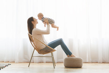 Mother sitting in chair and lifting her newborn child up