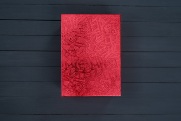 Red closed shiny cardboard box on a black wooden background. Top view. Present
