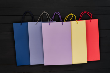 Five paper multi-colored shopping bags on black wooden background. Top view.