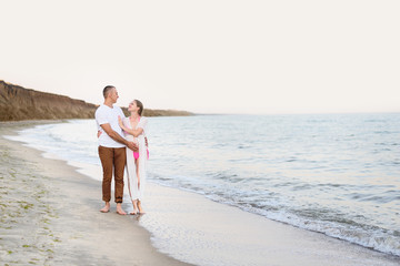 Young married couple walks along the sea coast. Pregnancy. Pre-sunset time