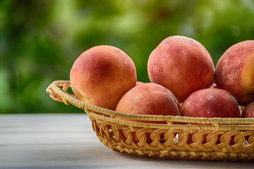 Ripe peaches in a wicker basket, green garden on the background. Close-up. Fruit season