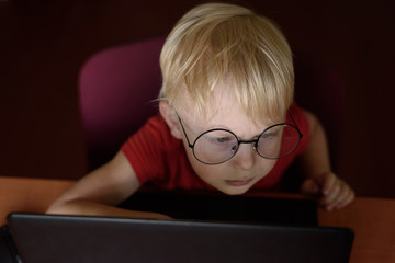 Portrait of a serious blond boy with glasses at a laptop. Top view
