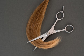 Cropped curl of blond and scissors. Black background. Close-up