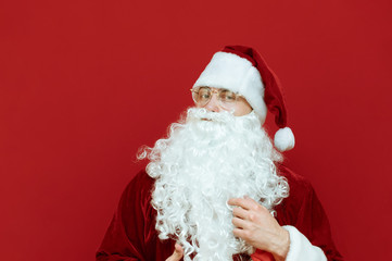 Fototapeta na wymiar Closeup photo of Santa Claus isolated on red background, wearing classic red suit and glasses, looking into camera. Christmas concept. Copyspace. Xmas