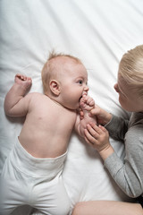 Baby and smiling older brother are lying on the bed. They play, communicate and interact. Top view