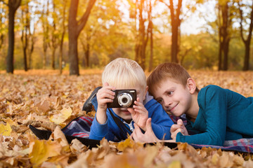 Two little brothers take a pictures on the camera. Lying in yellow autumn leaves. Fall day